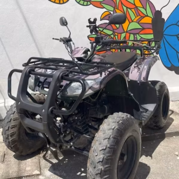 A four-wheeled ATV with large tires is parked by a wall painted with a colorful abstract mural of leaves and a butterfly.