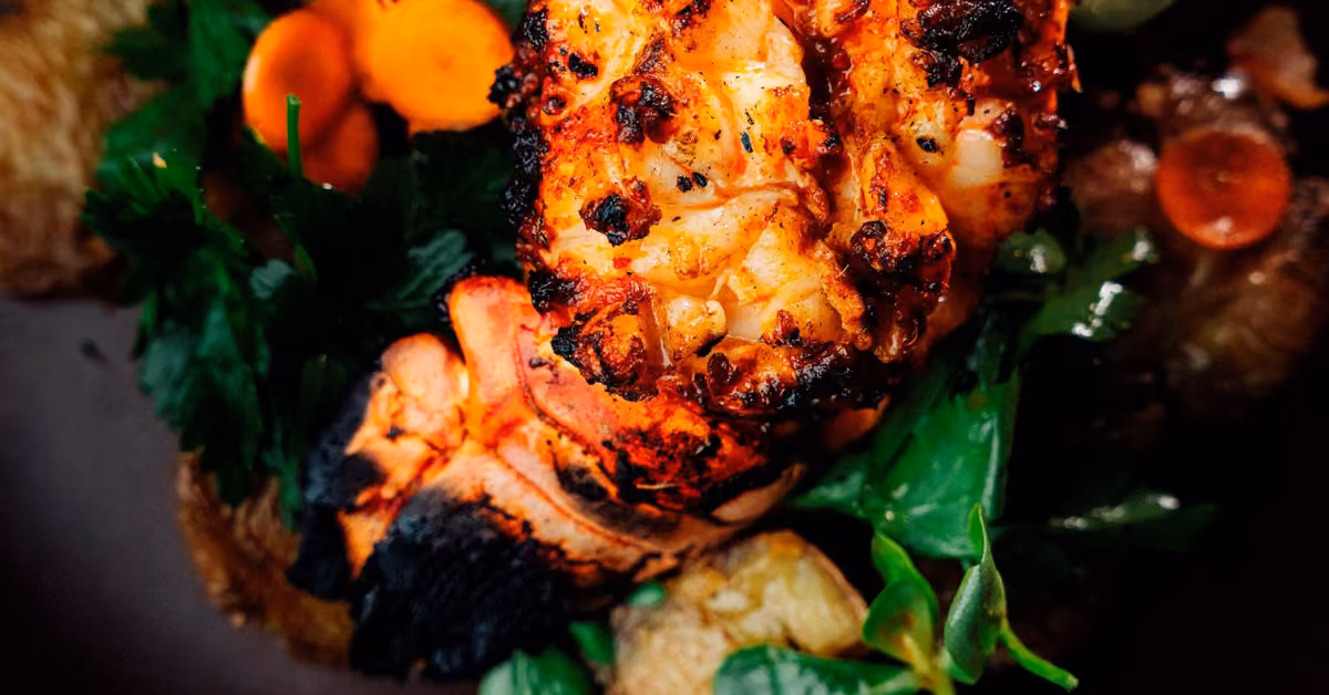 Grilled lobster tail with fresh herbs and sliced carrots, charred edges, and vibrant colors at BAK Restaurant.