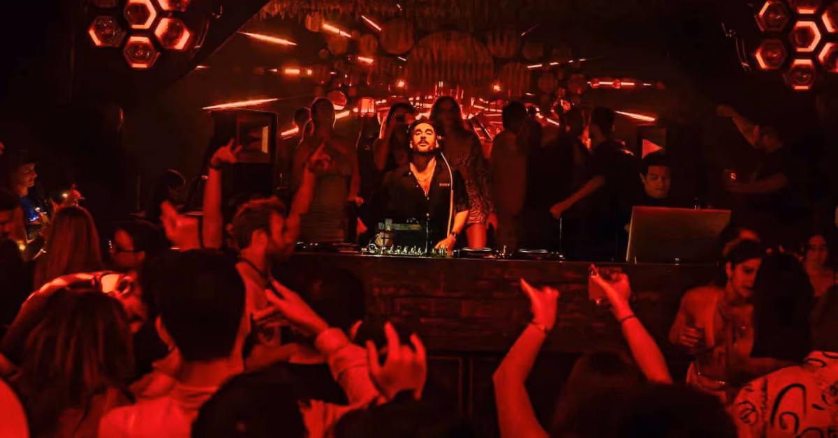 A DJ spins at Bonbonniere Night Club, surrounded by dancers and red lights, setting a lively, energetic mood.