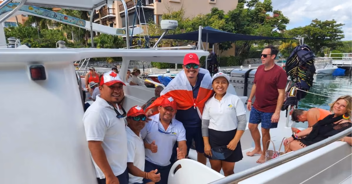 People in white uniforms and red hats pose for a photo on a docked boat, others nearby prepare for a catamaran sailing tour.