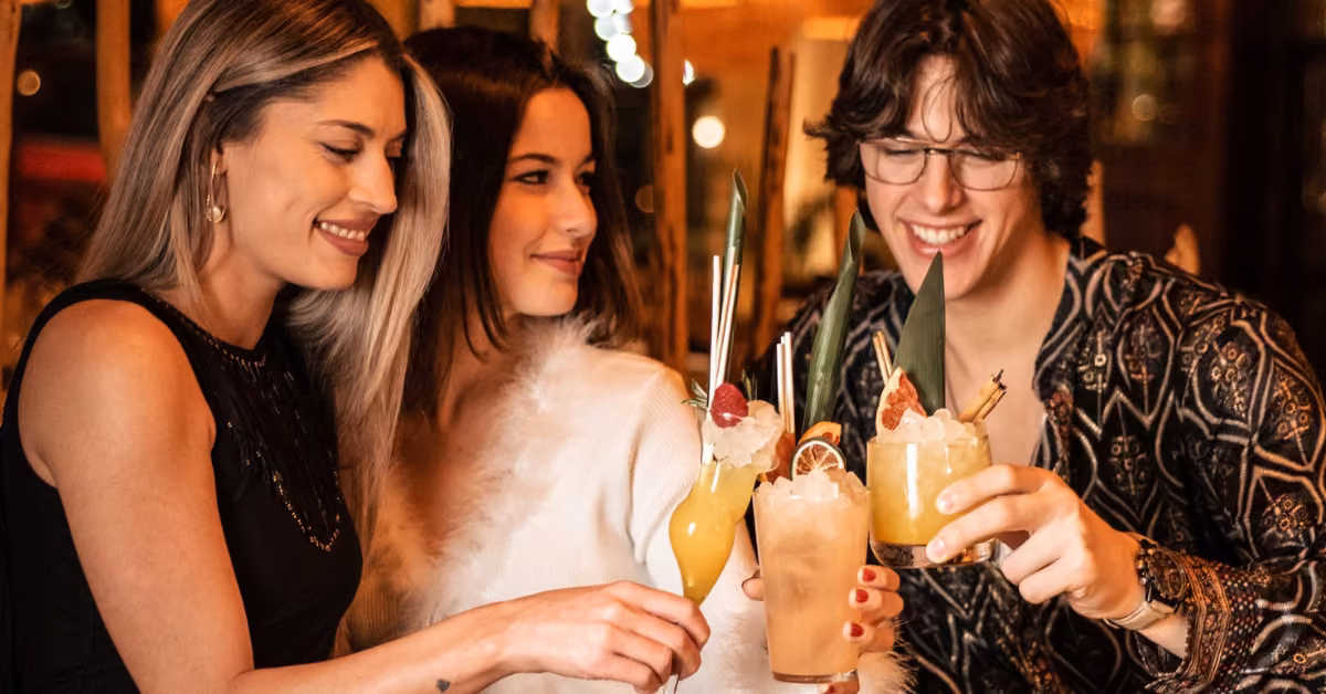 Three people smile and clink colorful cocktails at Chambao Restaurant, enjoying a festive night in a lively indoor setting.