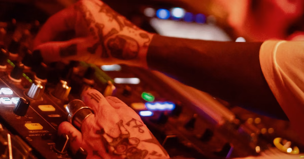 Tattooed hands adjust knobs on a DJ mixer at Confessions Night Club, colorful lights and blur hinting at a lively atmosphere.