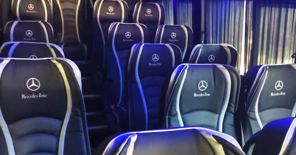 Black leather seats with Mercedes-Benz logos in rows, blue lighting, and dark curtains on bus windows.
