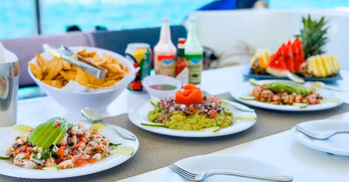 Table with ceviche, guacamole, chips, and sliced fruit is enjoyed on a cruise with an ocean view in the background.