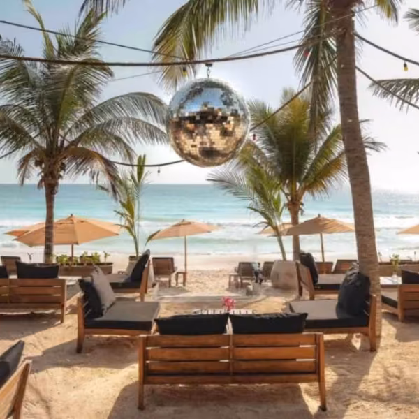 Gitano Beach Club lounge with wooden sofas, black cushions, disco ball, palm trees, umbrellas, and ocean under a sunny sky.