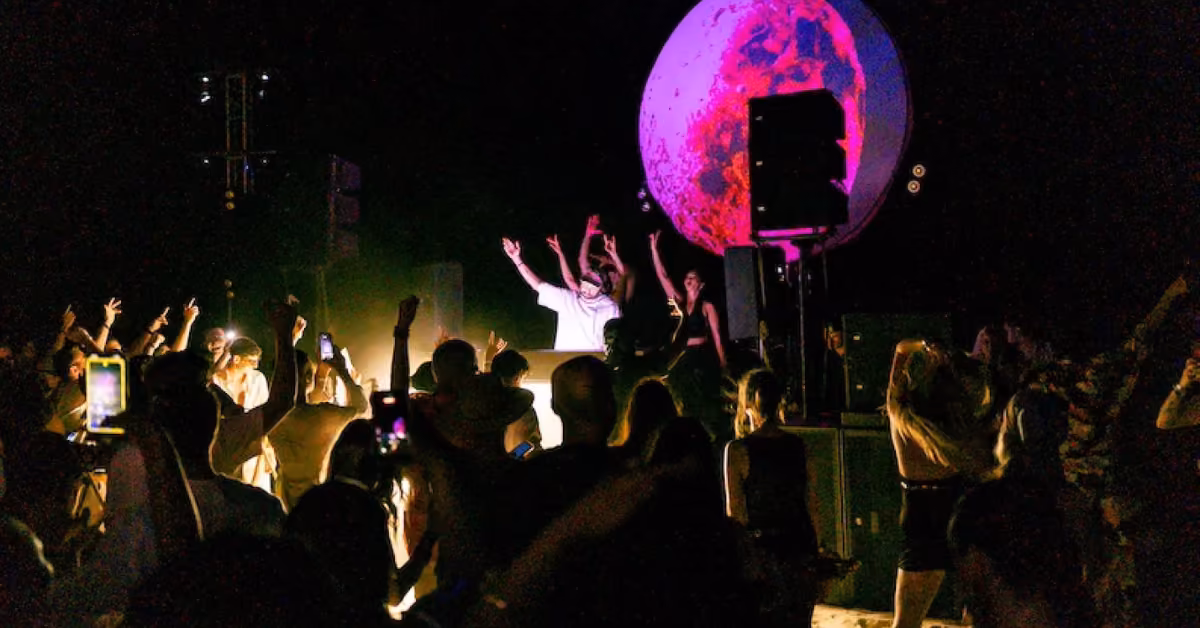 People dance with raised hands at a nighttime Gitano Beach Club concert, DJ on stage and glowing sphere in the background.