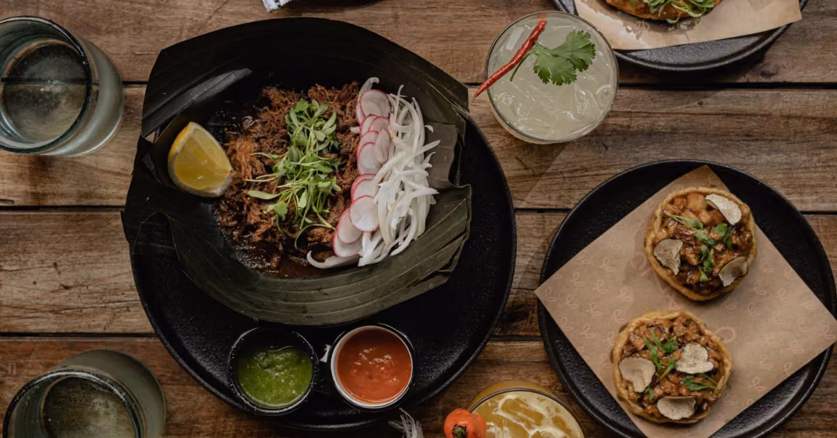 A table at Gitano Jungle Restaurant with shredded meat, radishes, onions, tacos, sauces, lemon wedge, and assorted drinks.