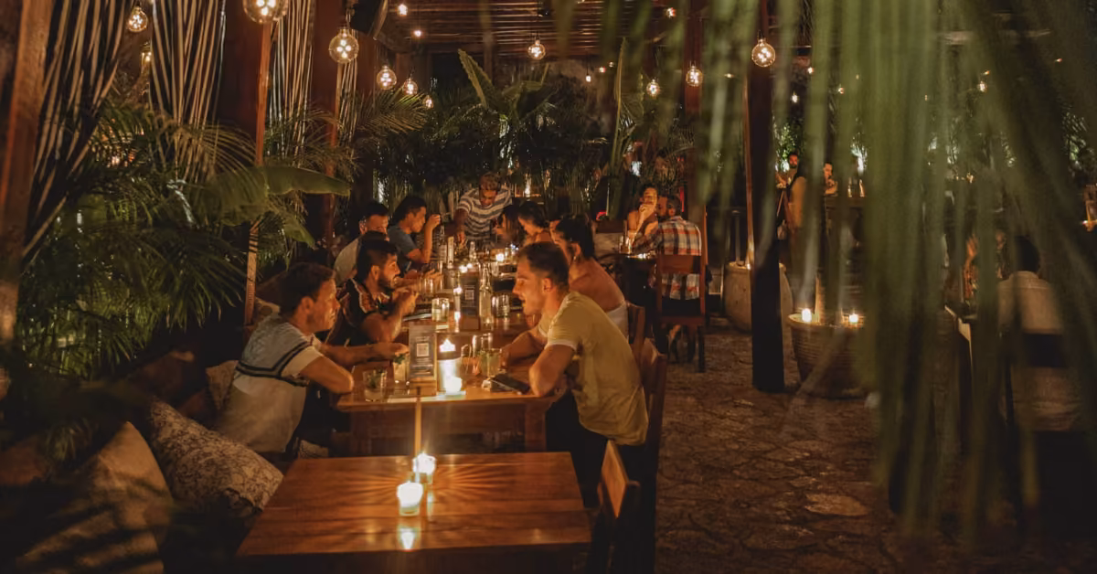 Guests dine at wooden tables by candlelight, surrounded by lush plants in Gitano Jungle Restaurant’s cozy, lively setting.