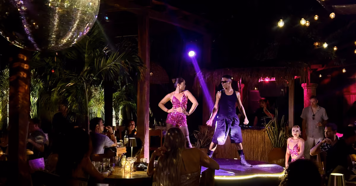 Two dancers perform under colorful lights at Gitano Jungle, with a disco ball overhead and palm plants around the lively bar.