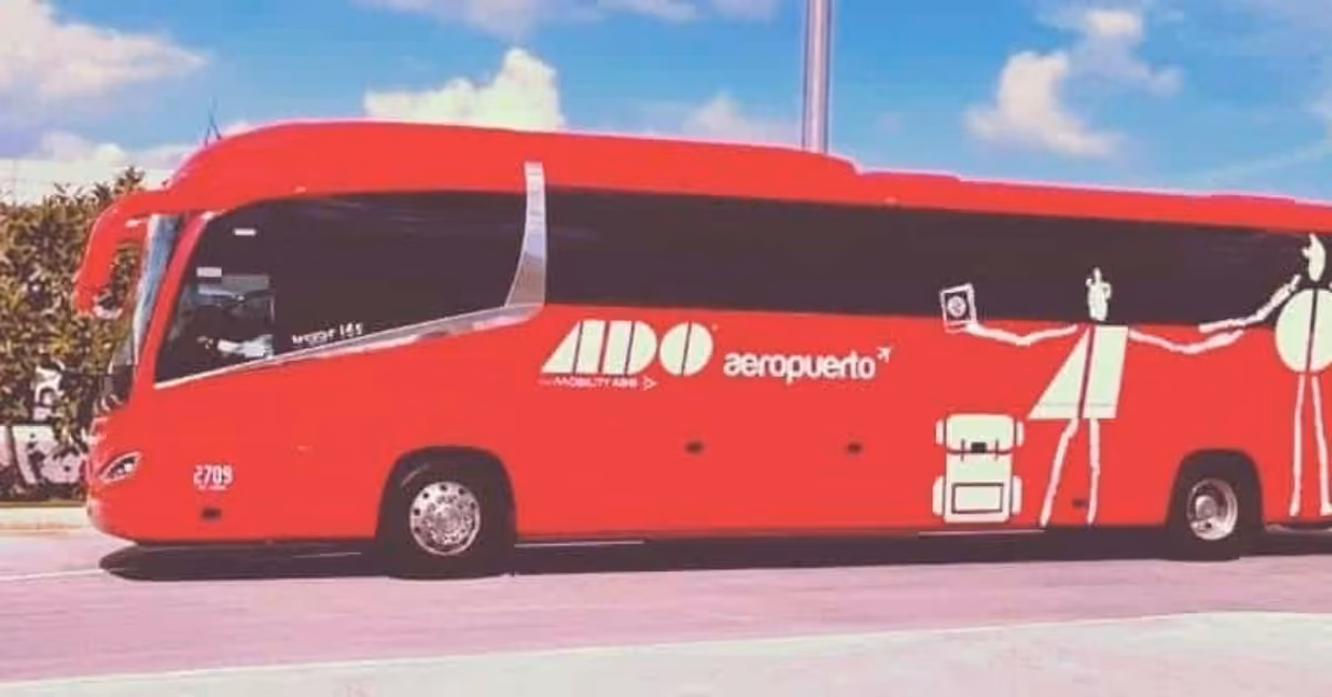 A red ADO Aeropuerto bus with white traveler graphics is parked in Tulum under a clear blue sky.