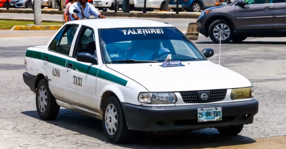 A white and green taxi with “TAXI” and the number 636 on the side drives down a city street among other cars.