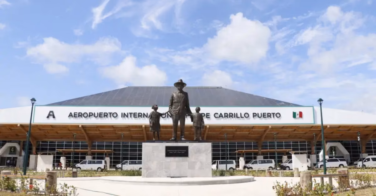 Felipe Carrillo Puerto airport with a three-figure statue, sign, Mexican flag, and partly cloudy sky near Tulum.