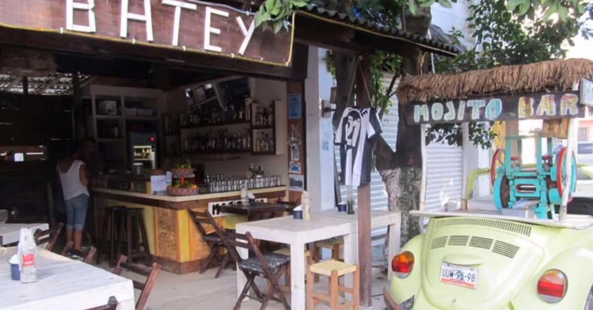 Outdoor bar with rustic tables, a green VW Beetle mojito bar under a thatched roof, and “Batey” sign overhead.