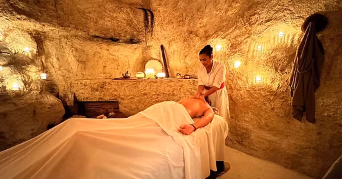A person gets a massage in a dimly lit, cave-like room with wall candles, creating a warm and soothing spa atmosphere.