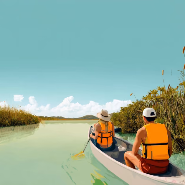 Two people in life vests paddle a canoe down a calm river lined with green plants under a clear blue sky with scattered clouds.