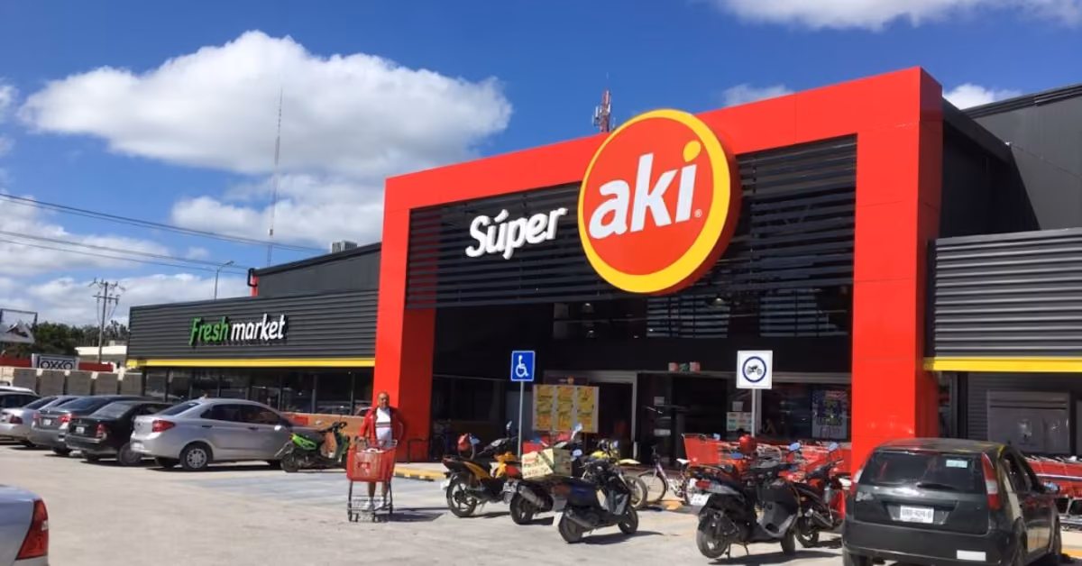 Súper Aki supermarket in Tulum with cars, motorcycles, and a person with a shopping cart in the parking lot under clouds.