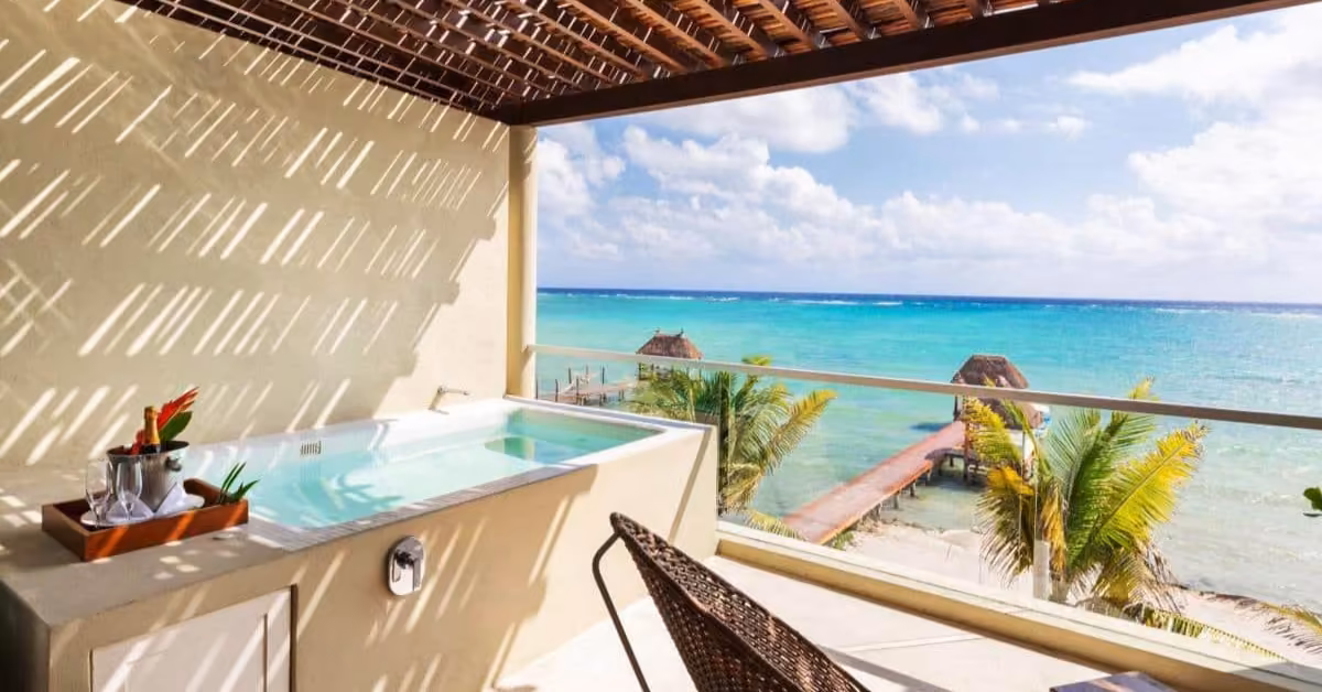 Tulum balcony with a small pool, ocean view, palm trees, lounge chair, drinks tray, and pergola shadows on the wall.
