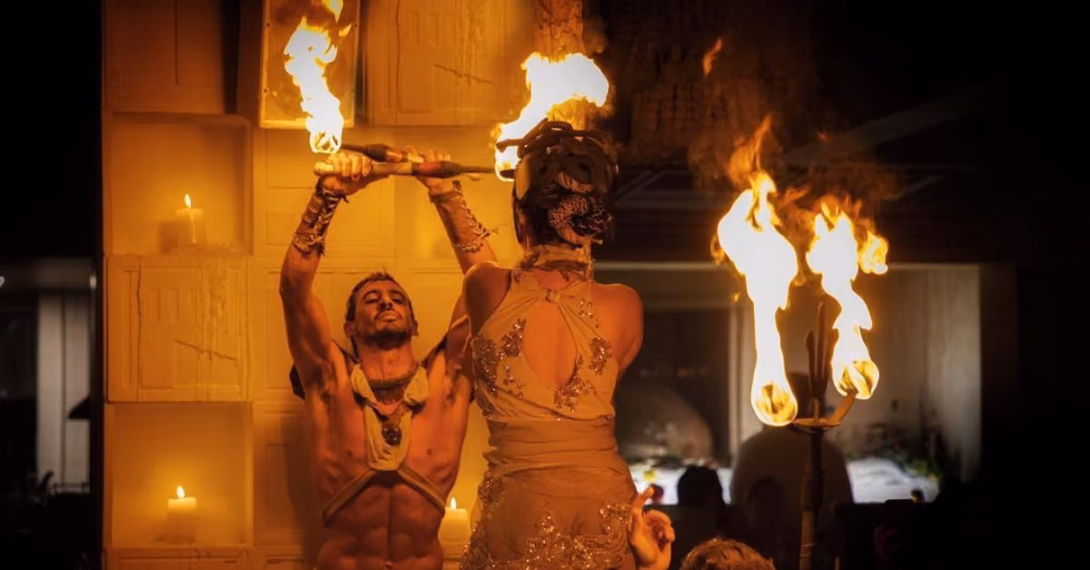 Two costumed performers with torches and a fire staff entertain at Ilios Restaurant, surrounded by candles and warm light.
