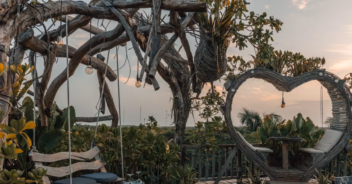 Wooden benches on the Karma Rooftop amid greenery and vines, with a heart-shaped frame and tropical plants at sunset.