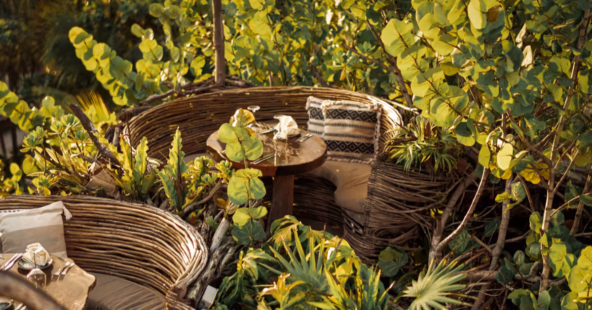 Cozy outdoor seating at Karma Rooftop with round wicker booths, lush plants, and a wooden table set for dining.