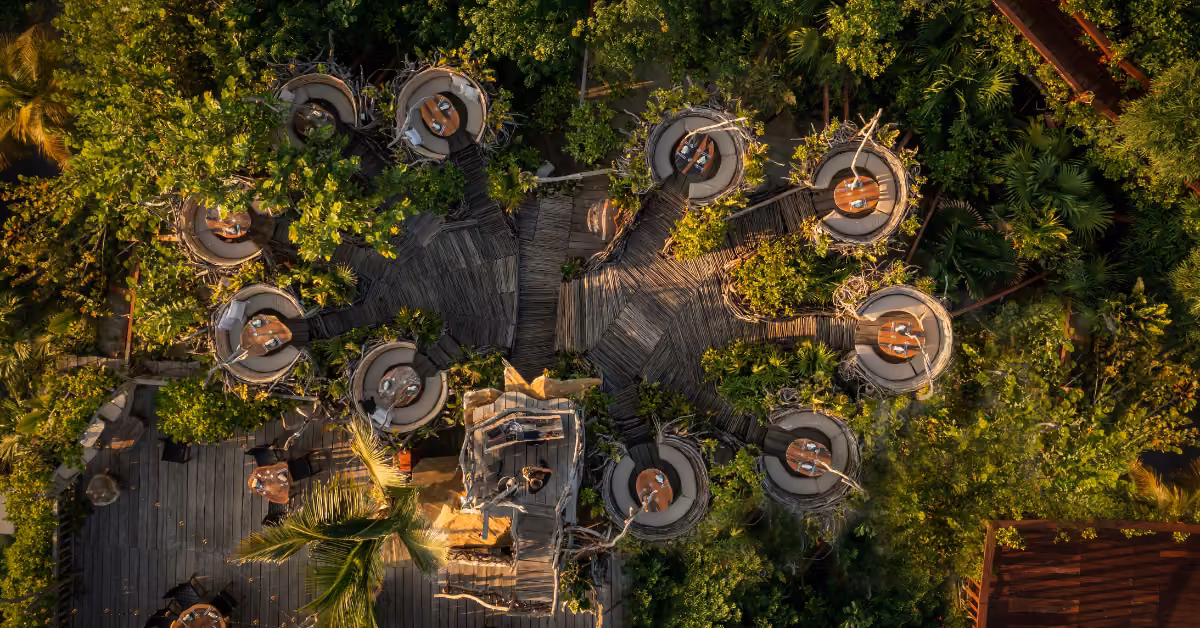 Karma Rooftop restaurant with circular dining pods among lush trees, linked by wooden walkways in a tropical garden setting.