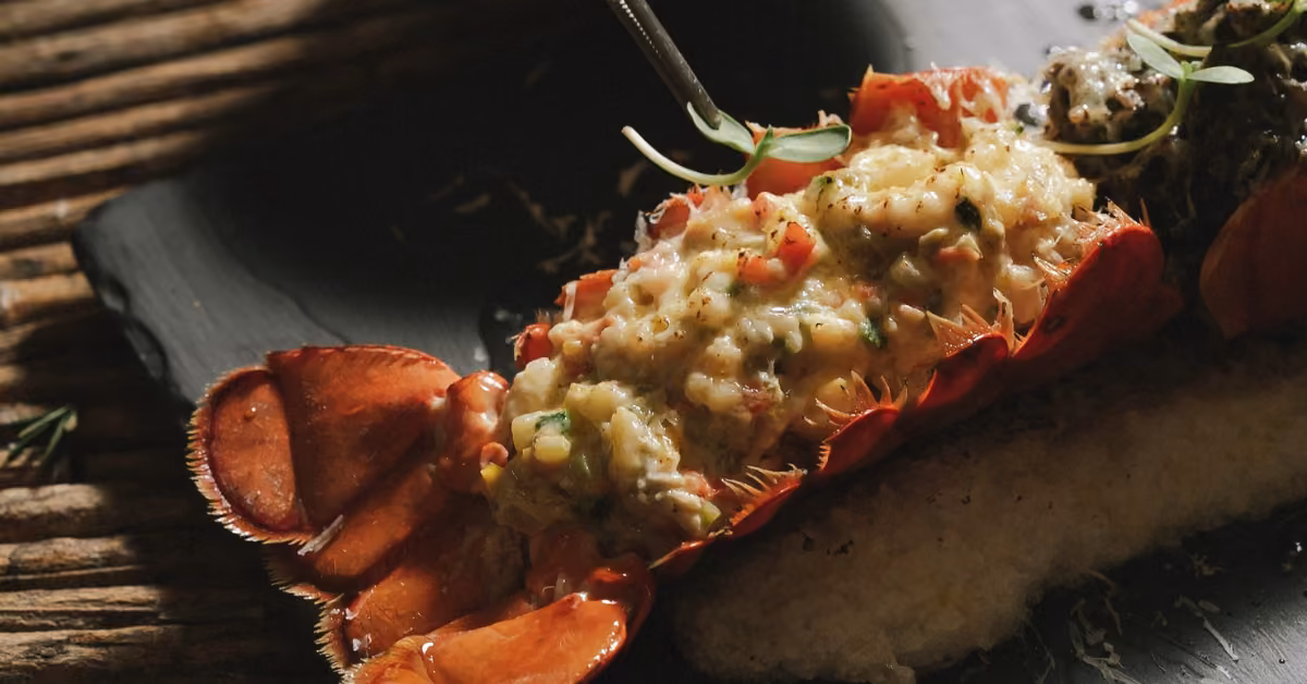 Lobster tail split open, filled with creamy seafood topping and microgreens, served on black slate for an elegant dinner.