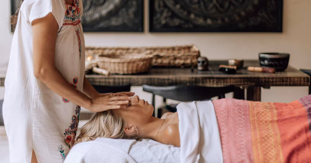 A woman receives a facial massage on a colorful towel in a peaceful room, with baskets and artwork decorating the background.