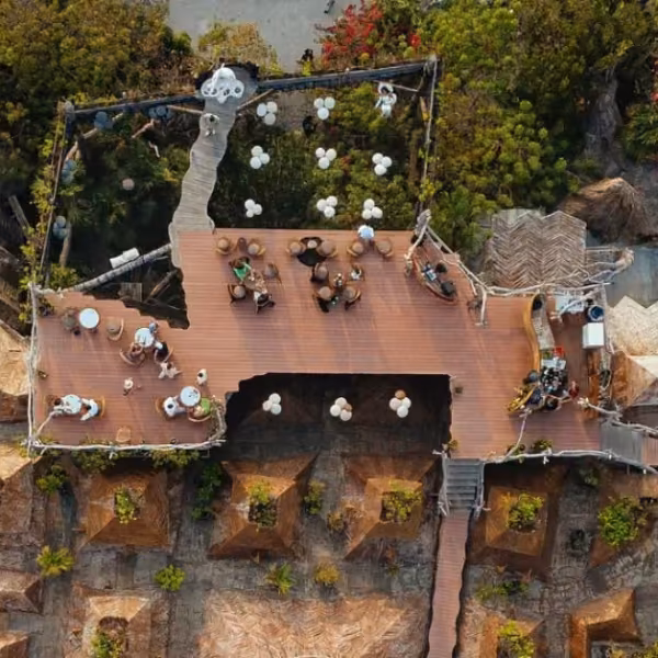 Rooftop café with tables and guests, nestled in lush greenery, winding paths, and rustic architecture woven with natural elements.