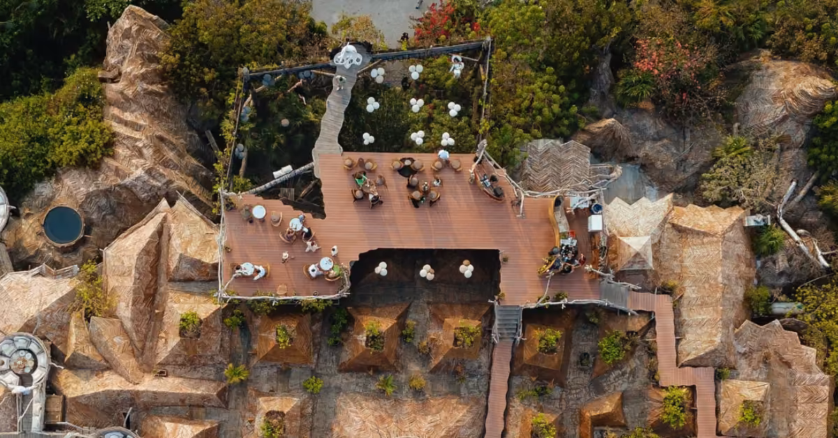Rooftop café with tables and guests, nestled in lush greenery, winding paths, and rustic architecture woven with natural elements.