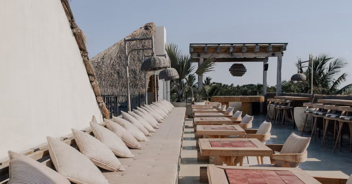 Panamera Rooftop features cushioned benches, wood tables, wicker lights, and tropical plants for relaxed outdoor dining.