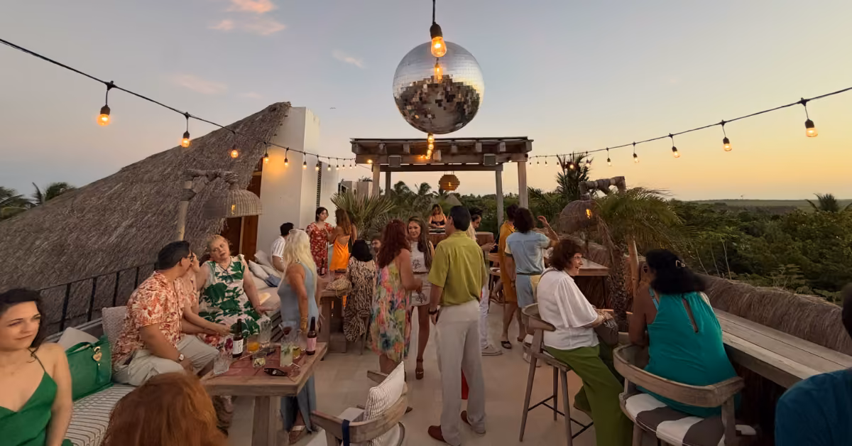 Guests mingle under string lights and a disco ball at sunset, enjoying the scenic view among palms on the Panamera Rooftop.