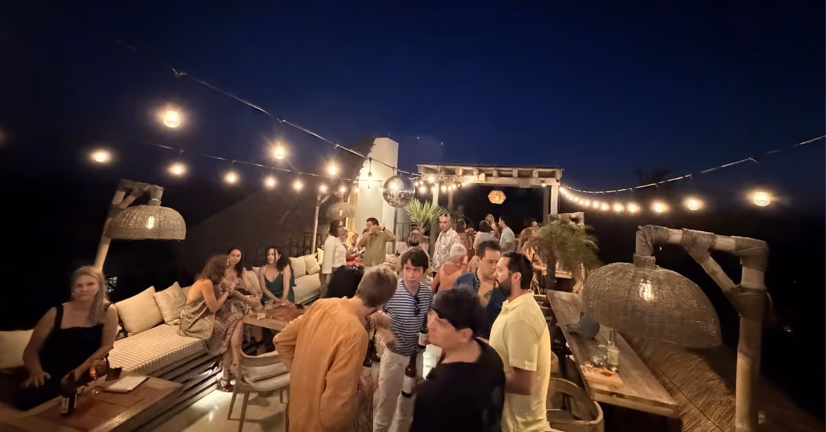 People gather and chat at Panamera Rooftop bar in the evening, surrounded by string lights, tables, and lush plants.