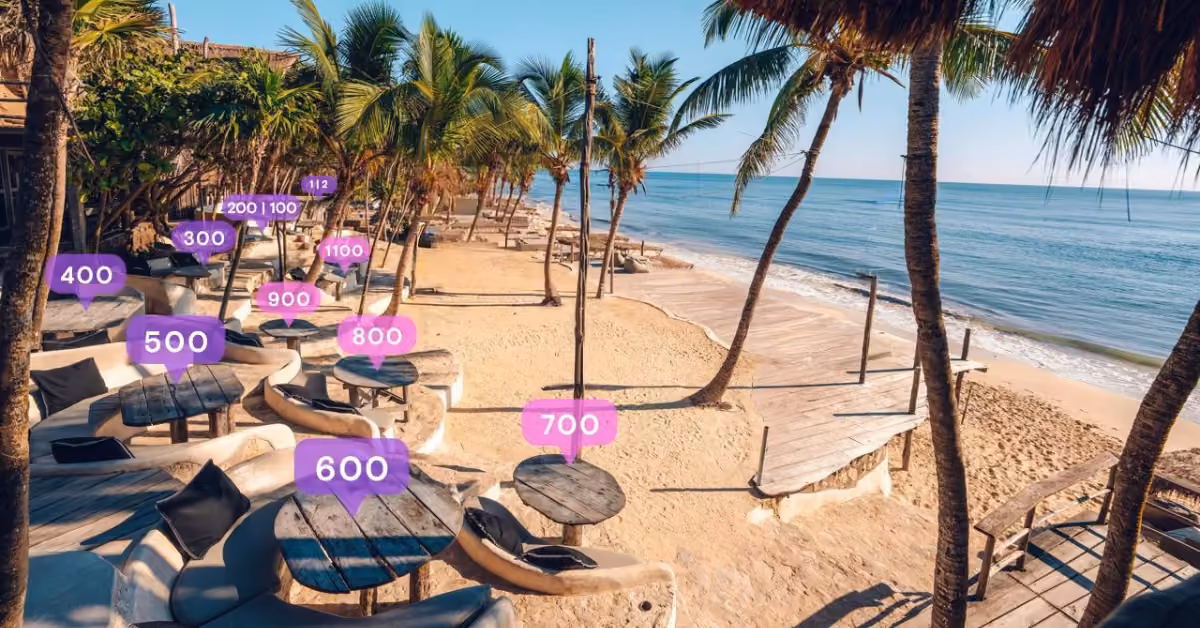 Beachside lounge with palm trees, white sand, round tables, and pink-purple notification icons above seats; calm ocean backdrop.