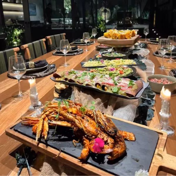 A wooden table with grilled shrimp, fresh salads, corn, elegant glassware, and candles creates a warm, inviting dining scene.
