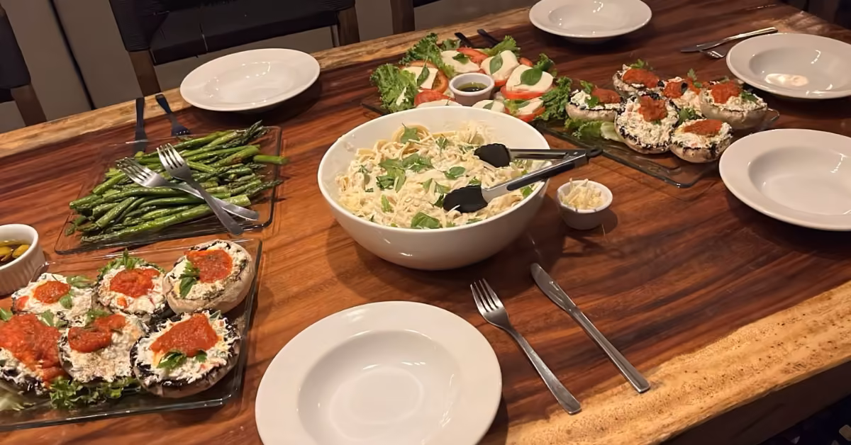 Table set for four with pasta, grilled asparagus, stuffed mushrooms in red sauce, and tomato-mozzarella salad.
