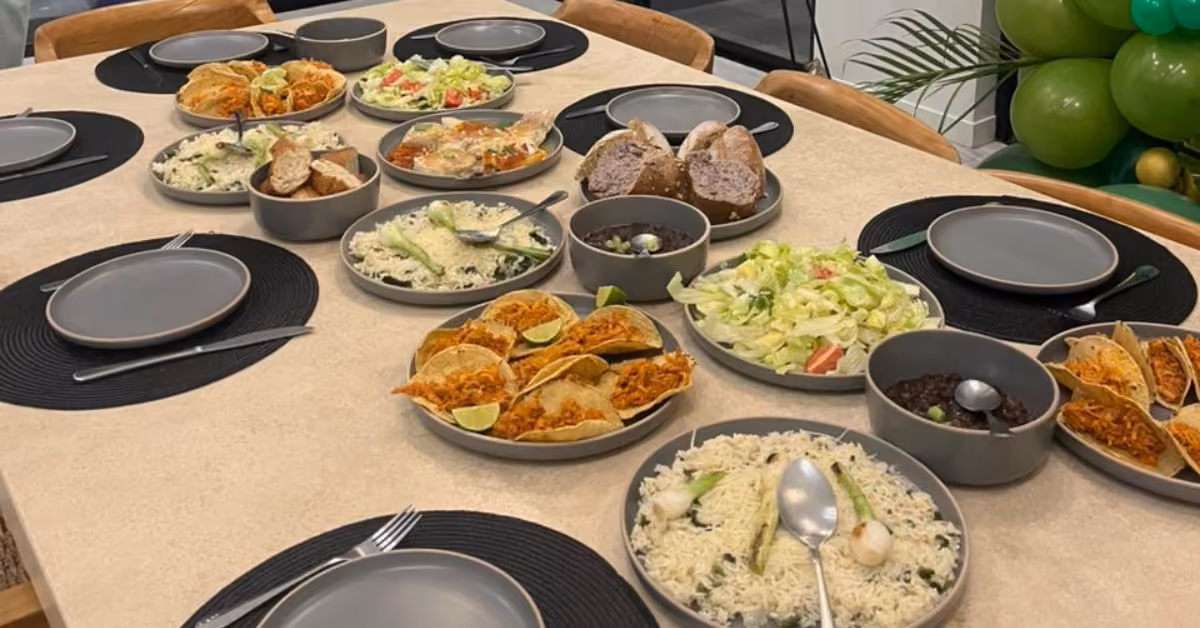 Table set for six with tacos, rice, salad, bread, side dishes by a private chef; green balloons in the background.