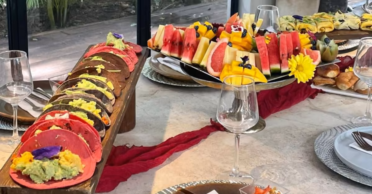 A chef’s table with vibrant tacos, fresh fruit, and pastries, decorated with edible flowers and elegant place settings.
