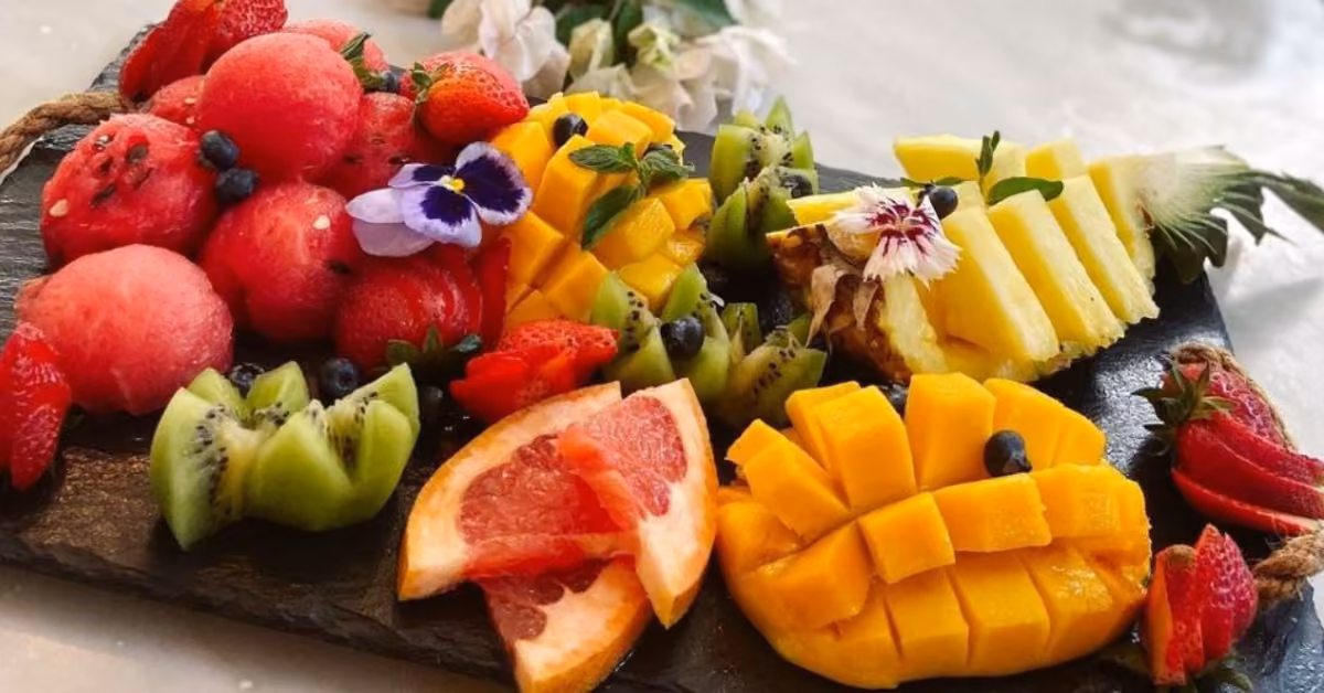 A vibrant fruit platter with mango, pineapple, kiwi, grapefruit, berries, and watermelon balls garnished with mint and flowers.