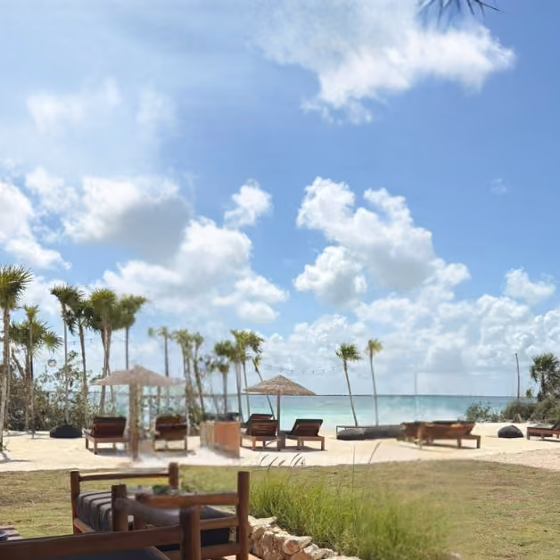 Unwind at Sipalitos Lagoon Club’s outdoor lounge with wooden chairs, umbrellas, palm trees, blue skies, and ocean views.
