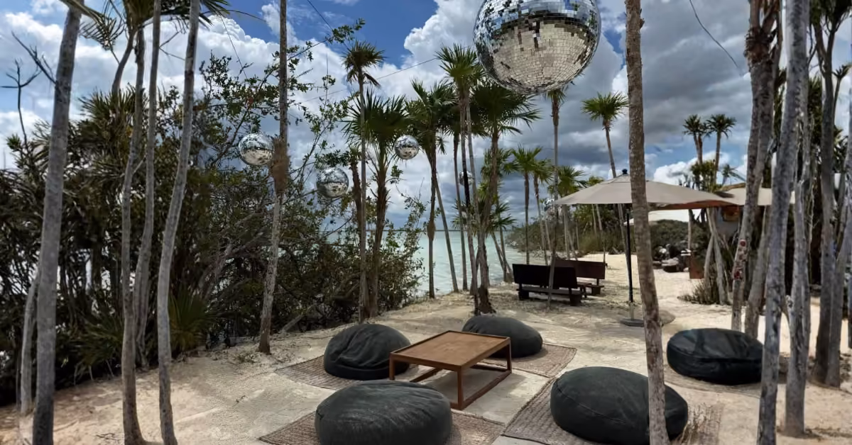 Beach lounge at Sipalitos Lagoon Club with low tables, black bean bags, palm trees, disco balls, and ocean views.