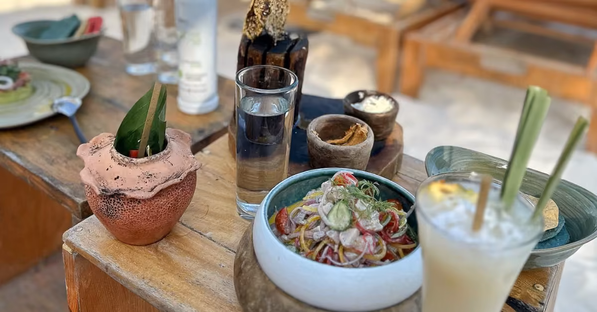 Outdoor table at Tantra Beach Club with salad, creamy lemongrass drink, clay pot with leaves, and small side dishes.
