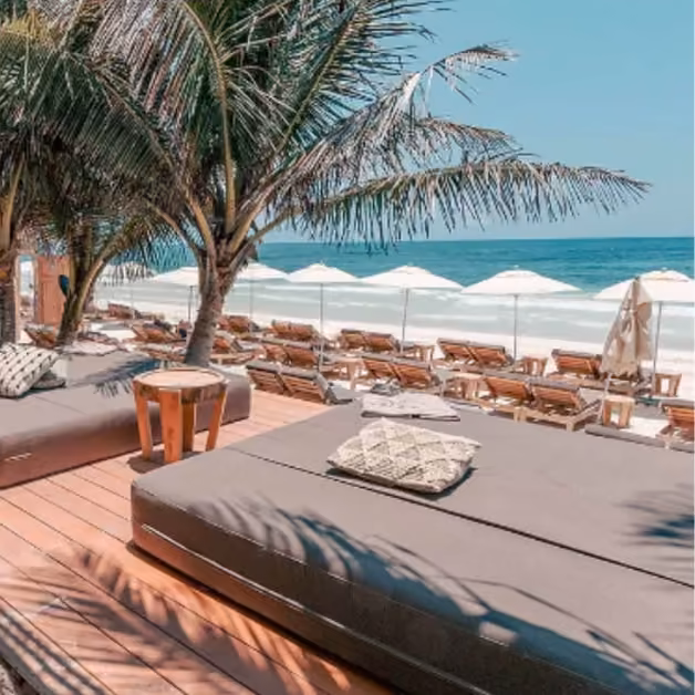 Tantra Beach Club’s lounge has cushioned daybeds, wooden decking, palm trees, and sun loungers with umbrellas by the ocean.