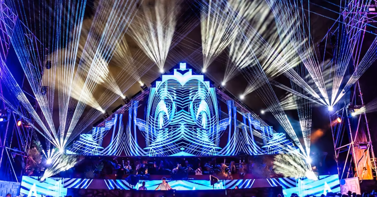 Night concert stage with vibrant blue-white LEDs, colorful lights, and beams shooting upward at Tehmplo Music Festival.