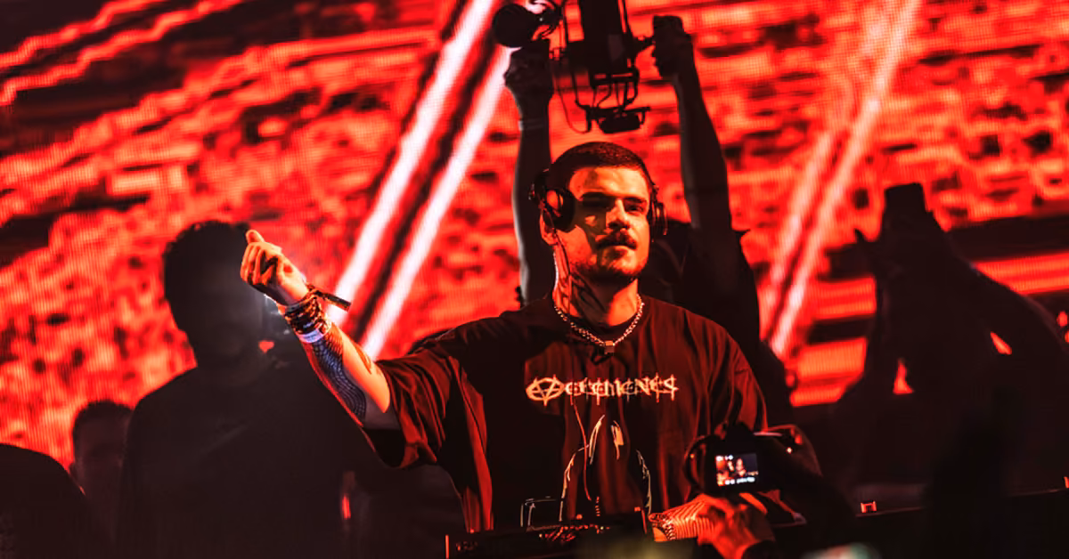 A DJ in headphones and a black T-shirt performs at Tehmplo Festival, red lights and abstract visuals glowing behind him.