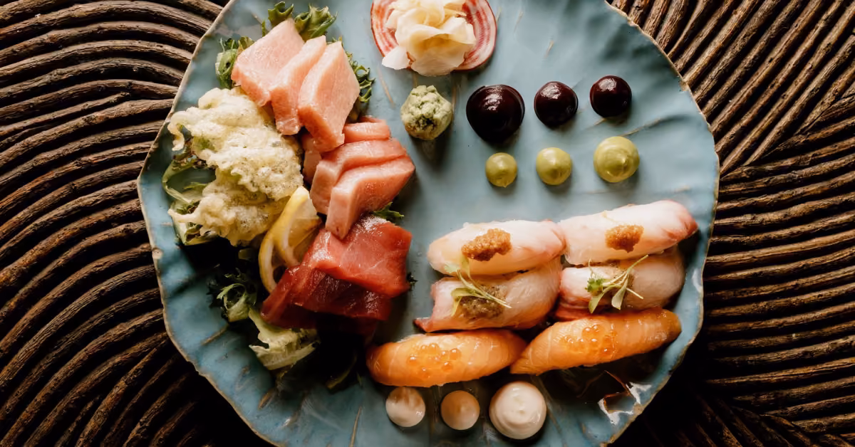 Assorted sushi, sashimi, and nigiri garnished with wasabi, sauces, and pickled ginger on a woven surface at Tseen-Ja Rooftop.