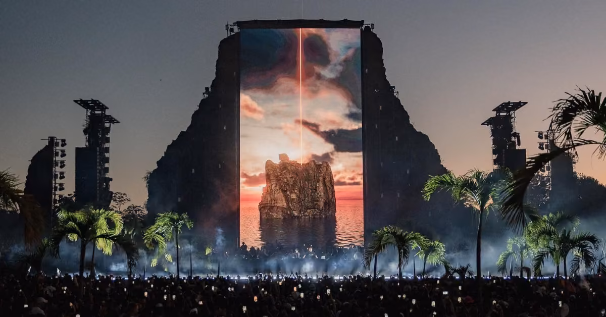 Crowds enjoy an outdoor Zamna Music Festival at dusk, palm trees framing the stage and a vibrant island scene on the big screen.