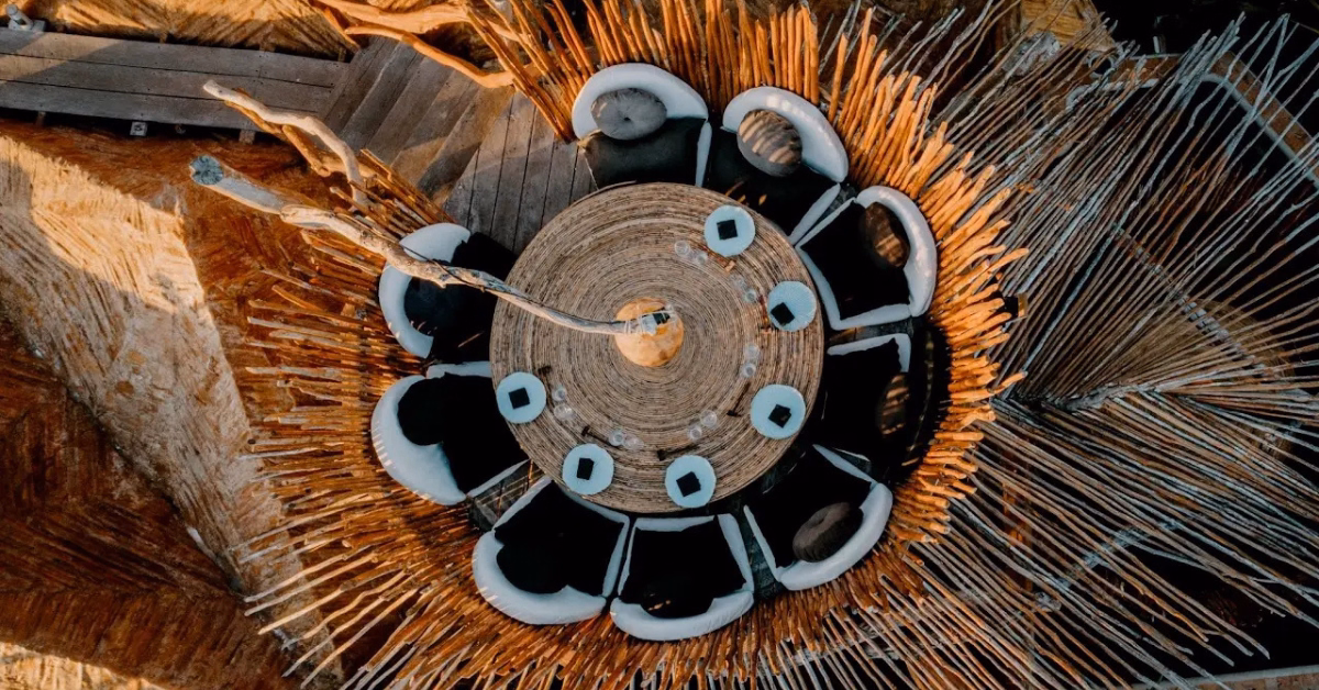 Aerial view of a circular wooden table surrounded by black and white chairs, set on the tseen-ja rooftop deck with radiating wooden slats creating a striking sunburst pattern.