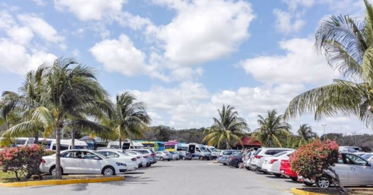 Cars parked in a lot bordered by palm trees and bushes under a partly cloudy sky in Tulum.