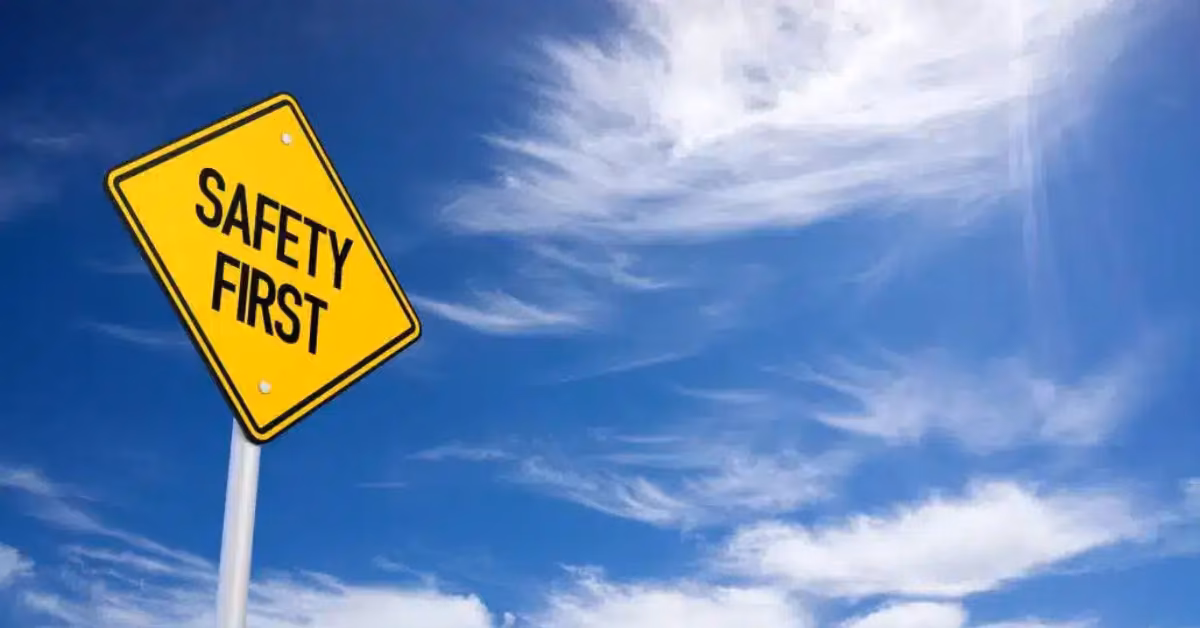 A yellow Safety First sign stands against a bright blue sky with white clouds, reminding travelers to stay aware.