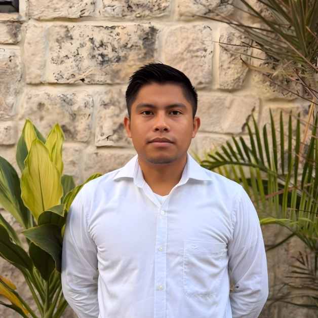 A man with short dark hair in a white shirt stands before a stone wall, flanked by green plants, looking calm and professional.